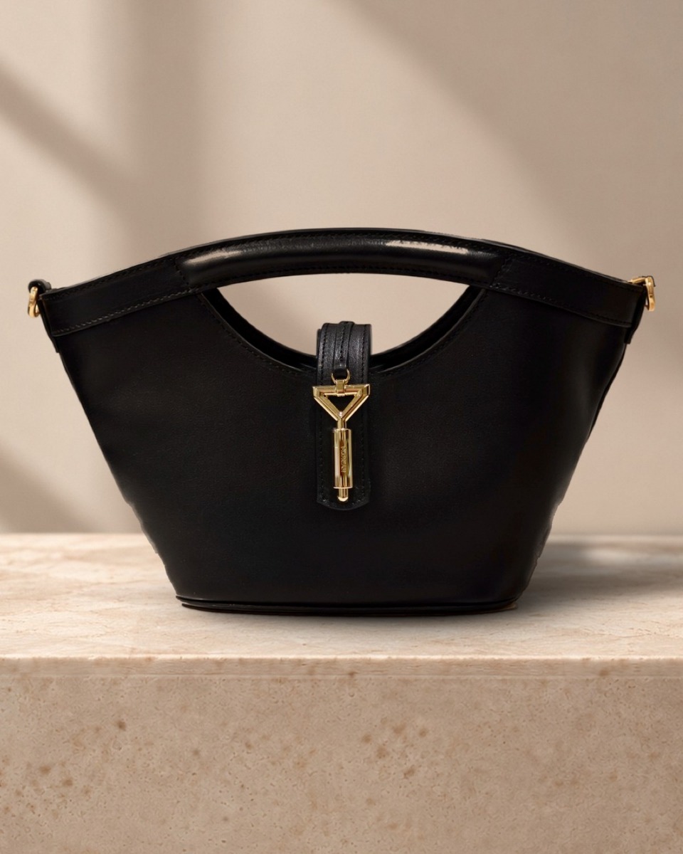 Closer view of the Heidi Tote: smooth black calf, stitched tab and gold triangle clasp engraved FLORIAN, in warm window light
